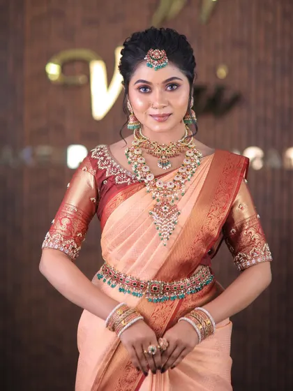 A full set from a photoshoot featuring a lovely peach-colored silk saree. The drape is kept simple and elegant to highlight the beautiful color and the intricate temple jewellery.