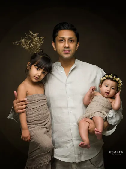 A father holds his two children in this artistic family portrait. The dark, moody background makes the subjects stand out beautifully.
