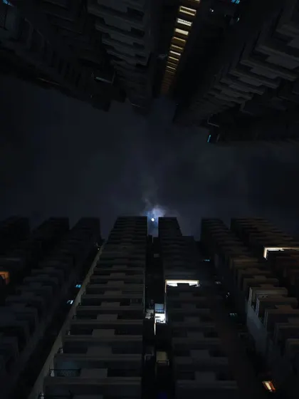 A similar low-angle shot of city buildings, but at night. The composition creates a moody, almost dystopian feel, framed by the dark silhouettes of the architecture.