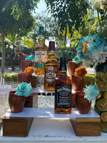A beautiful daytime bar setup featuring premium whiskies like The Glenlivet and Chivas Regal. The display is accented with fresh flowers, creating an elegant and inviting look for an outdoor event.