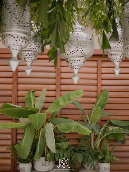A backdrop of wooden shutters is enhanced by hanging silver Moroccan lanterns and lush banana plants, creating a tropical yet sophisticated look.