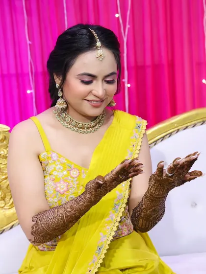 The bride admiring her intricate henna. The makeup is designed to complement the festive and colorful vibe of the event.