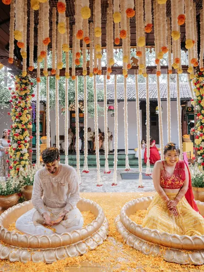 The couple sits inside the lotus-shaped urlis during their Haldi ceremony, sharing a laugh as they are covered in flower petals.
