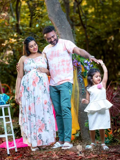 A happy family of three enjoying a moment together during an outdoor maternity shoot. The daughter dances while her parents watch, capturing the joy and anticipation of their growing family.