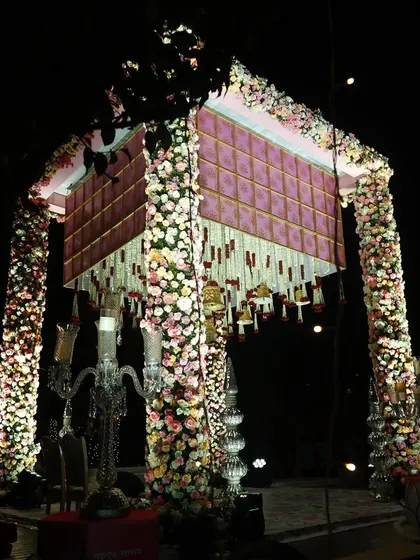 A magnificent floral mandap at night. The structure is covered in thousands of pastel-colored flowers, and when lit up, it creates a truly magical and breathtaking sight for an evening ceremony.