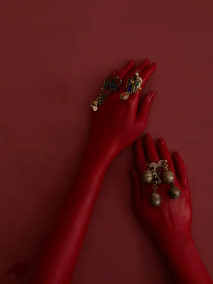 Another artistic detail shot of the jewellery on the red-painted hands. This composition is clean and minimalist, allowing the intricate designs of the rings to stand out as the central focus.