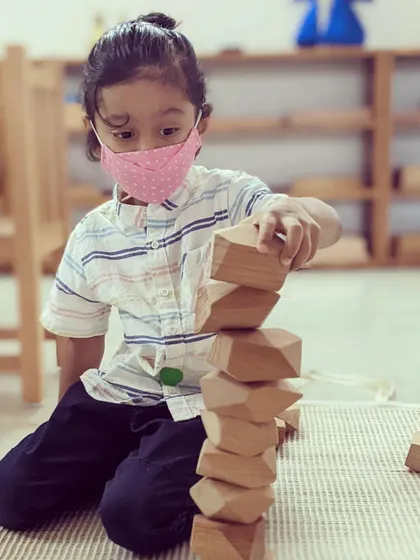 A child carefully stacks wooden balancing blocks, an open-ended material that encourages concentration, creativity, and an intuitive understanding of physics and balance.
