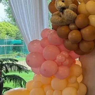 A teddy bear appears to be climbing a column of pink and brown balloons, adding a playful and dynamic element to the decor.