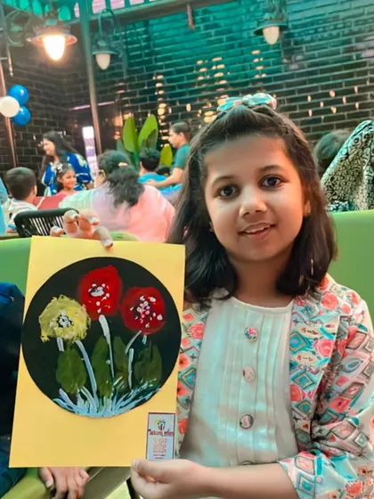 A happy guest proudly holding up the floral artwork she created using bubble wrap and leaf impression techniques. Each child gets to explore different textures and methods.