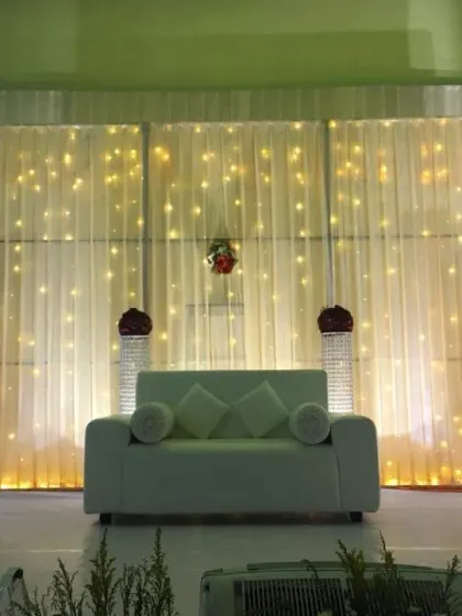 A minimalist and modern stage with a simple white sofa, illuminated pillars, and a backdrop of sparkling fairy lights.