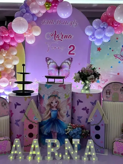 A close-up of the butterfly-themed cake table area, showing the detailed graphics on the plinths and the light-up name display.