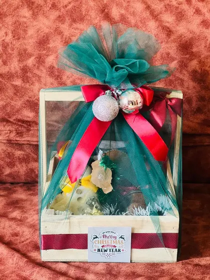 A festive Christmas and New Year hamper in a wooden crate, wrapped in green tulle with a red ribbon and decorative baubles.