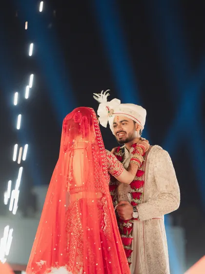 This close-up captures the intimate moment of the varmala exchange. Even with the grand pyrotechnics in the background, the focus remains on the couple's happy and emotional connection.