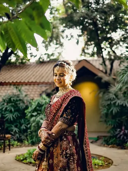 A beautiful outdoor portrait of the bride in her wedding lehenga. The natural setting and her serene expression create a peaceful and elegant image.