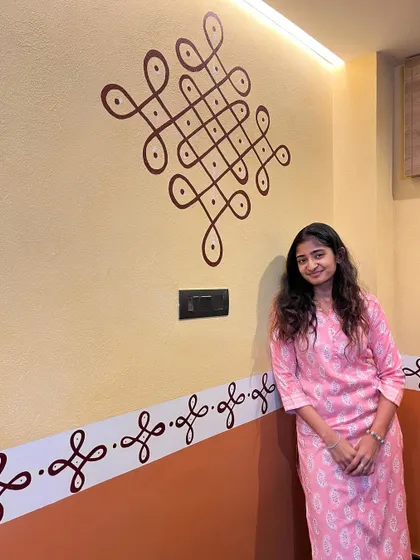 Standing proudly next to the completed traditional rangoli wall art. The combination of the larger motif and the delicate border pattern creates a balanced and beautiful design for the entrance.