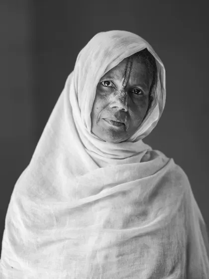 A black and white portrait of a woman from the "Widow Holi" celebration in Vrindavan. Her expression is one of quiet dignity and resilience.