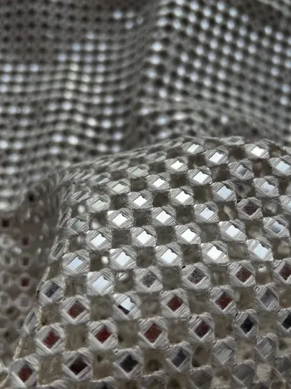 This silver embroidered cutwork fabric with mirror details offers a dazzling and sophisticated look, perfect for gowns and blouses.