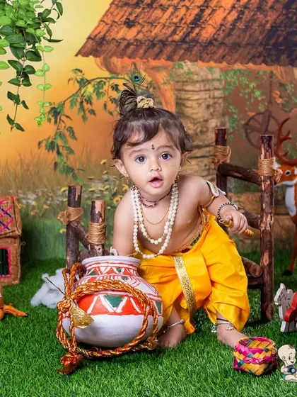 An expressive shot of a baby boy dressed as Krishna, surrounded by props like a pot of butter and toy deer. His curious look is what makes this themed photo so special.