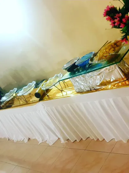 A side view of a buffet table with clean white skirting and a gold runner. The glass-top risers add a modern touch to the food display.