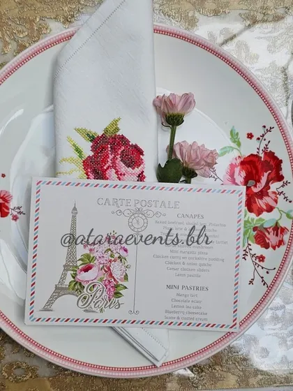 An elegant place setting from a Paris-themed baby shower. The plate features a floral design, and the menu is designed like a vintage postcard from Paris.