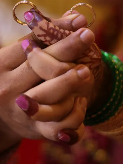 An intimate shot of a couple's intertwined hands, showcasing their wedding rings and the bride's mehndi.
