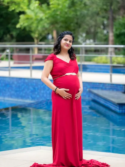 A lovely solo portrait of a mom-to-be in a red dress, posing by a swimming pool.