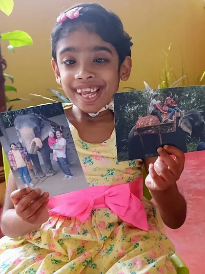 A child excitedly shares photos from her trip, including an elephant ride. These show-and-tell sessions build confidence and public speaking skills.