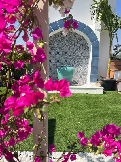 The vibrant pink of a bougainvillea vine beautifully frames the blue Moroccan fountain. This composition of color and form highlights how planting can be used to enhance and soften architectural features.