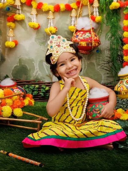 A joyful portrait of a little Radha with a big smile, surrounded by the vibrant colors of the Janmashtami theme.
