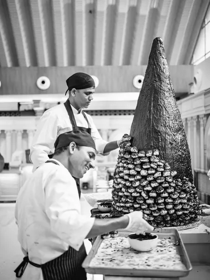 A black and white photo of our chefs smiling while building a croquembouche tower.