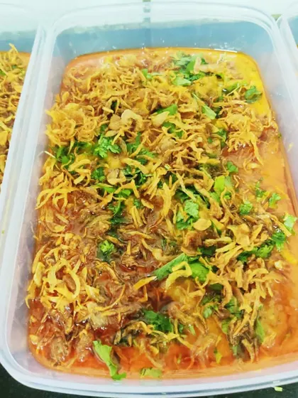 A takeaway container of our Mutton Khichda, garnished with fresh cilantro and crispy fried onions. It's a complete meal in itself, rich and satisfying.
