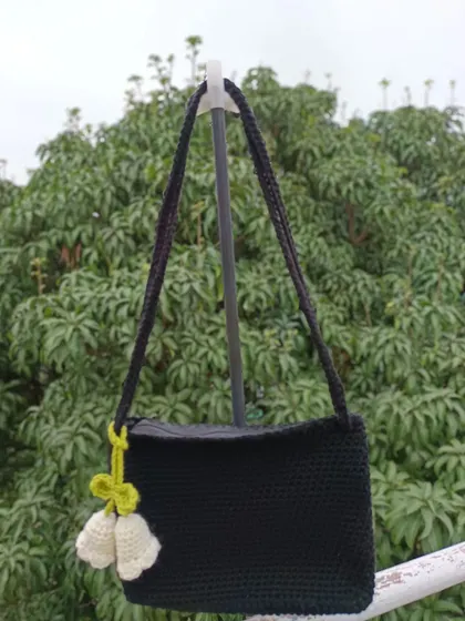 A custom black shoulder bag with a white tulip charm. The contrast of the black bag with the light charm makes for a striking design.