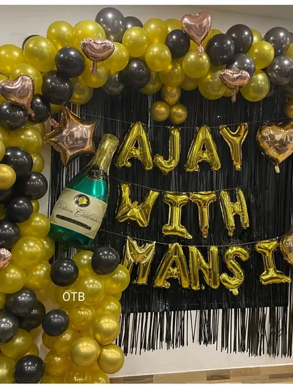 A straight-on view of the personalized anniversary decoration. The black fringe curtain makes the gold balloons pop, creating a glamorous photo booth area for the couple and their guests.