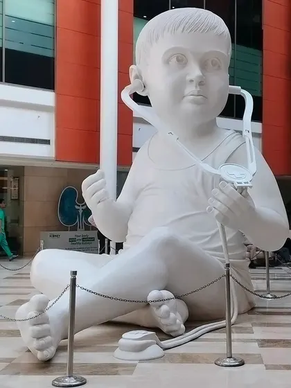 A frontal view of the giant baby sculpture, showing the detail in the hands and the stethoscope. This piece was crafted in sections and assembled on-site.