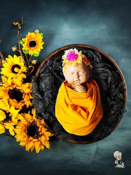 A newborn baby wrapped in a warm yellow swaddle, nestled in a dark bowl and accented with bright sunflowers. The contrast between the dark background and the vibrant yellow creates a stunning visual.