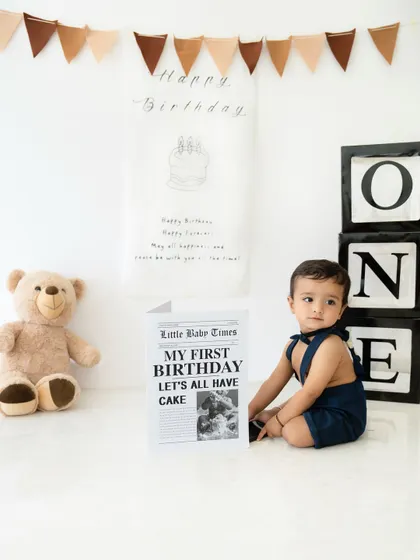 A modern and clean first birthday setup with a "Little Babe Times" newspaper prop. This theme is perfect for capturing classic portraits before the cake smash.
