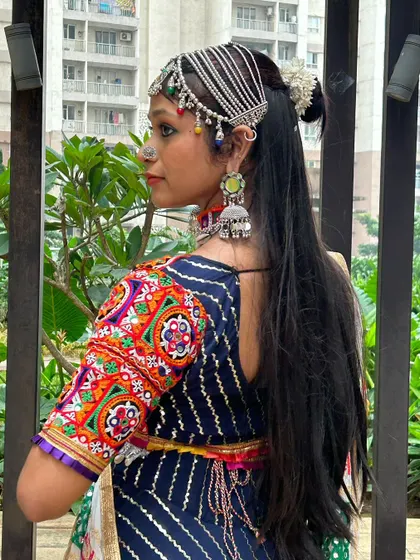 A side profile showcasing the intricate matha patti, jhumkas, and choker paired with a colorful embroidered blouse.