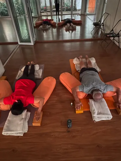 Two students in a supported prone Savasana, using bolsters and blocks for deep release. This highlights the quiet, meditative aspect of our classes.