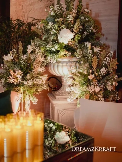 A classic stone urn overflowing with white and green florals, placed next to a comfortable lounge area. This detail adds a touch of timeless European garden elegance to the decor.