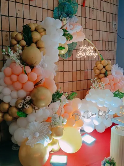 A classy and elegant birthday setup with a circular balloon arch in peach, white, and gold tones.