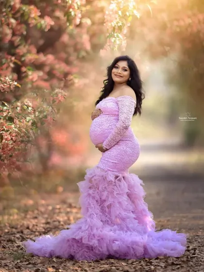 A fairytale moment in a sun-drenched lane. This lavender mermaid-style maternity gown features delicate lace sleeves and a dramatic ruffled train. It hugs the body to beautifully showcase your baby bump.