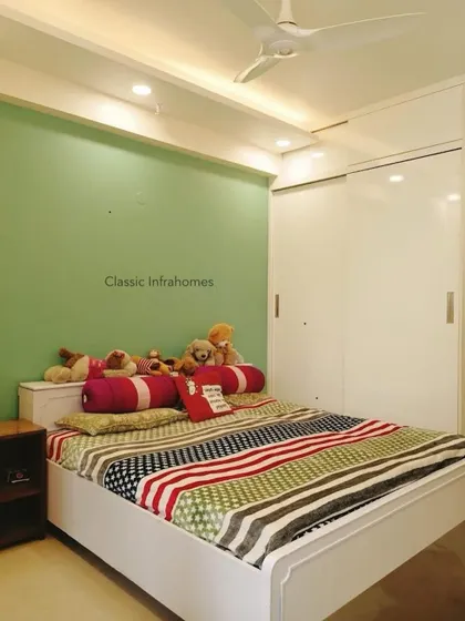 A simple and clean bedroom design from our Great Value Sarnam project. The room features a pastel green accent wall, a white sliding wardrobe, and a bed with colorful, cozy bedding.