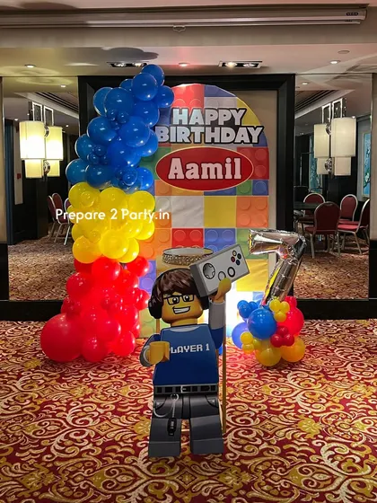 A fun Lego theme for a seventh birthday. This decoration uses primary colors, a Lego block backdrop, a large Lego figure cutout, and a silver foil number balloon to build the perfect party.