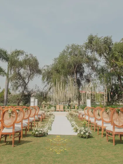 The view down the aisle, lined with elegant chairs and white floral arrangements, leading to a stunning mandap area under the trees. This is outdoor elegance at its finest.