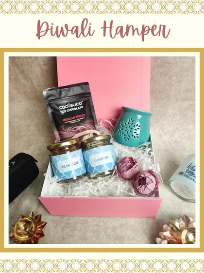 A cozy Diwali hamper perfect for a relaxing evening. It includes Mexican spiced hot chocolate mix, jars of almonds and cashews, and a ceramic diffuser, all in a lovely pink box.
