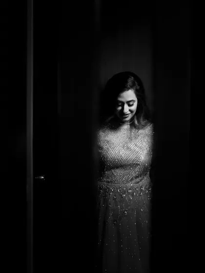 A mysterious and alluring black and white portrait of a bride peeking through a gap. The shadows create a sense of anticipation while highlighting her gentle smile.