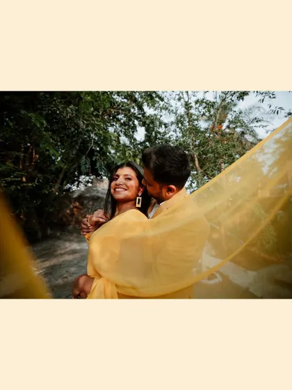 A romantic and dreamy shot of the groom kissing the bride's cheek, her yellow saree creating a soft, translucent veil around them.