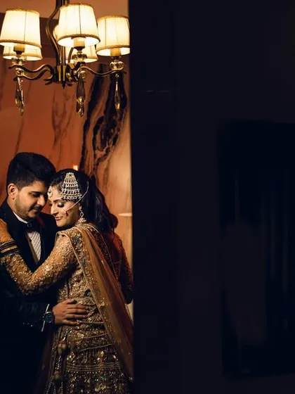 A beautifully framed shot of the couple sharing a slow dance in a warmly lit room. The composition, looking in from a dark foreground, creates a sense of privacy and intimacy.