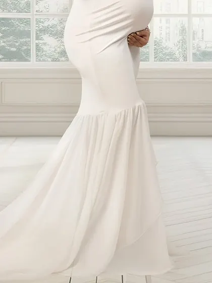 A close-up of a beautiful white mermaid-style maternity gown. The flowing train and the way it accentuates the baby bump make it a perfect choice for an elegant photoshoot.