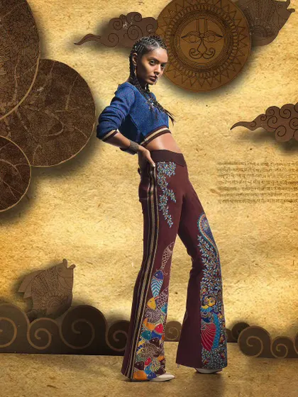 A dynamic pose highlighting flared trousers with elaborate embroidery. This shot from a designer catalogue focuses on movement and the unique silhouette of the pants against a creative, layered background.